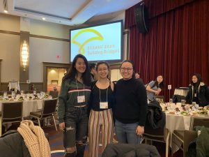 Three people standing in from of a screen reading ECAASU 2020 Building Bridges in a banquet hall